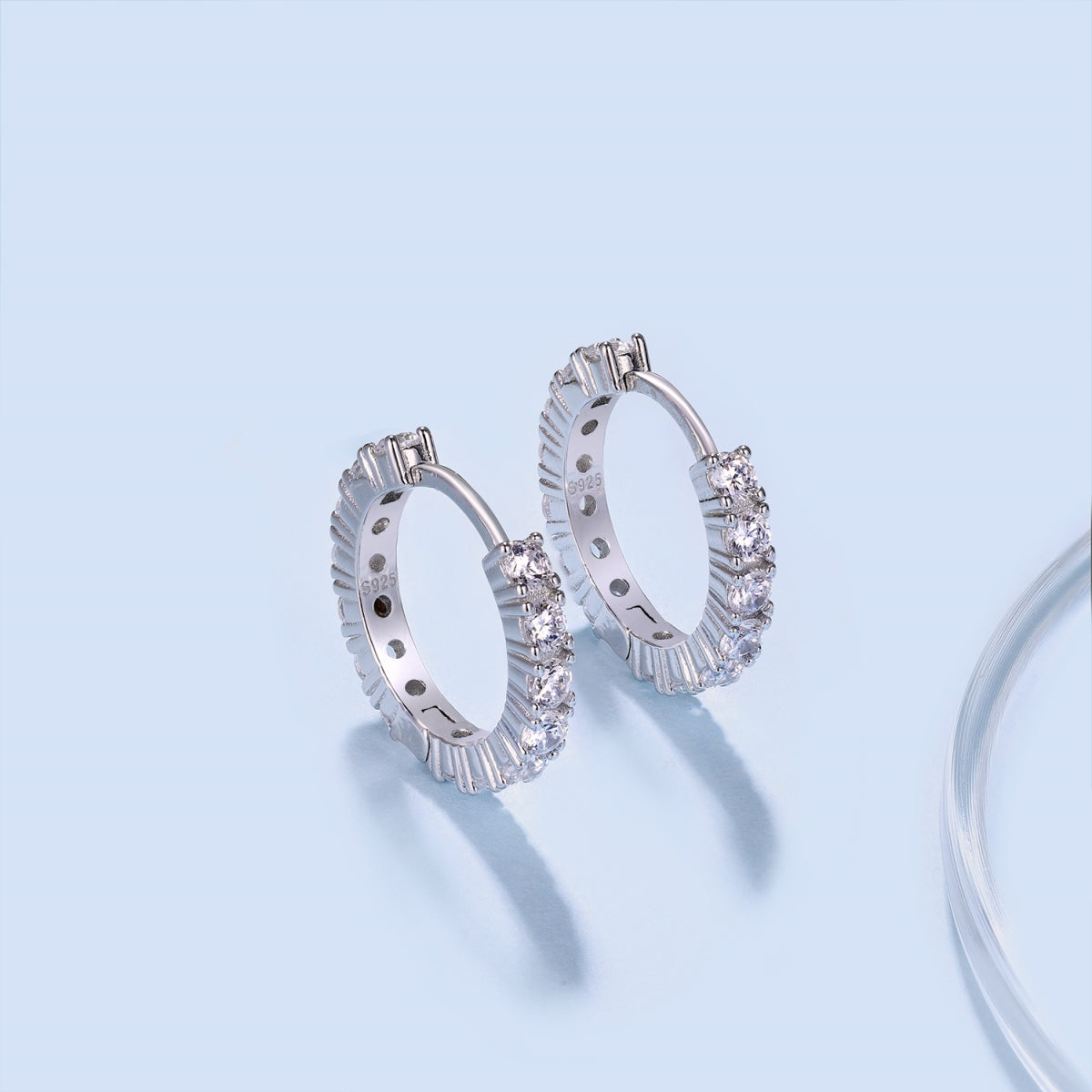 Silver hoop earrings with clear gemstones on a light blue background