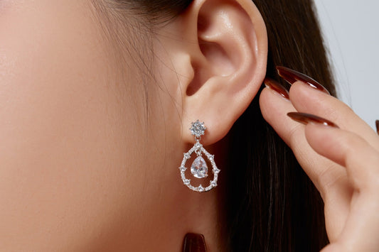 Person wearing a teardrop-shaped earring with a hand adjusting it.