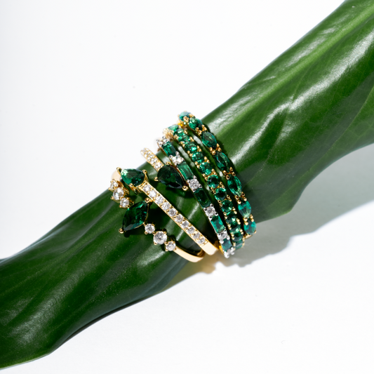 Emerald green stackable gold plated CZ rings collection featuring Zamradaa, Najma, Fajer, Rawan, Zamradi designs on green leaf - Luméra Designs Kuwait