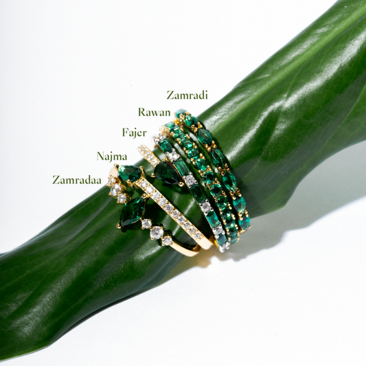 Emerald green stackable gold plated CZ rings collection featuring Zamradaa, Najma, Fajer, Rawan, Zamradi designs on green leaf - Luméra Designs Kuwait