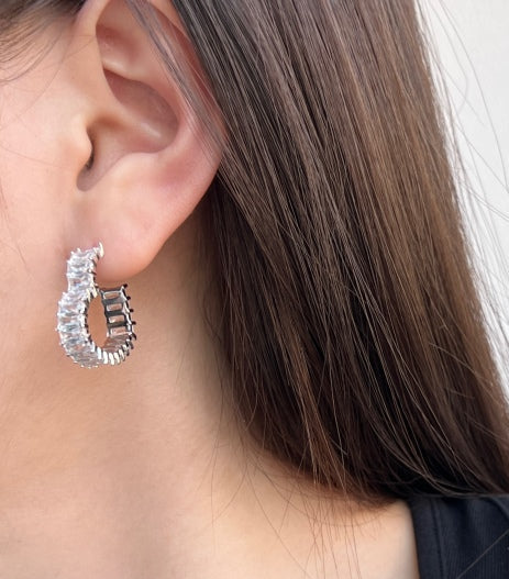 Close-up of a person wearing silver hoop earrings with a plain background
